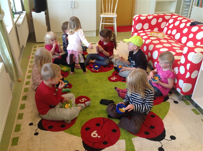 Flera barn som sitter i en cirkel på golvet och äter frukt