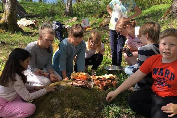 skolbarn utomhus i en halvcirkel där de lägger upp mat i skålar